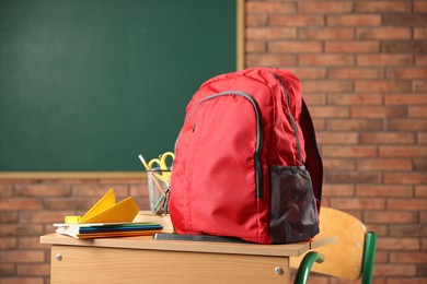 Photo of Red backpack, different stationery and paper plane on desk in classroom