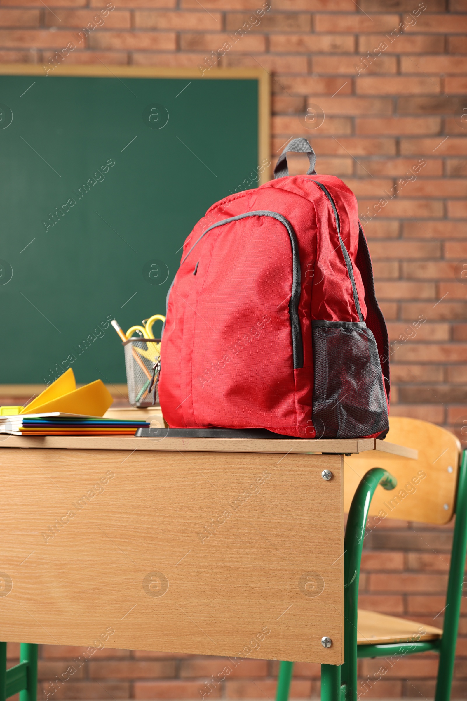 Photo of Red backpack, different stationery and paper plane on desk in classroom