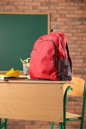 Photo of Red backpack, different stationery and paper plane on desk in classroom