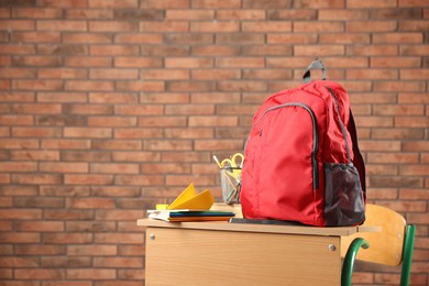 Photo of Red backpack, different stationery and paper plane on desk in classroom