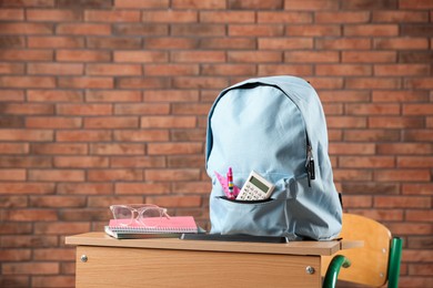 Photo of Light blue backpack with different stationery and glasses on desk in classroom