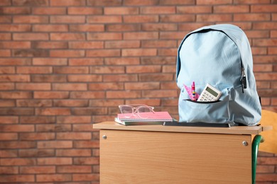 Photo of Light blue backpack with different stationery and glasses on desk in classroom. Space for text