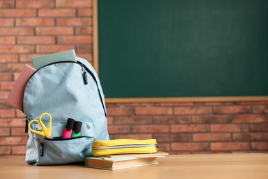 Photo of Light blue backpack with different stationery, pencil case and book on desk in classroom. Space for text