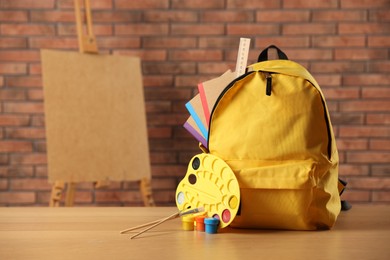 Photo of Yellow backpack with notebooks and art supplies on desk in classroom