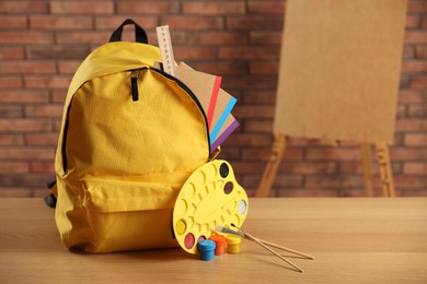 Photo of Yellow backpack with notebooks and art supplies on desk in classroom