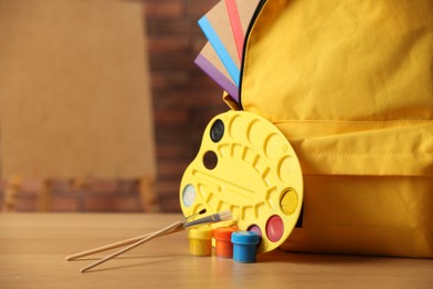 Photo of Yellow backpack with notebooks and art supplies on desk in classroom, closeup. Space for text