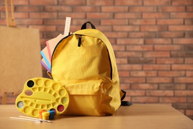 Photo of Yellow backpack with notebooks and art supplies on desk in classroom