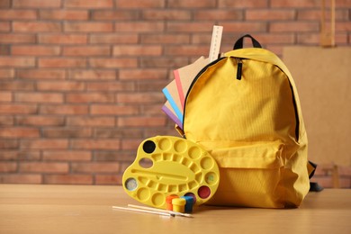 Photo of Yellow backpack with notebooks and art supplies on desk in classroom