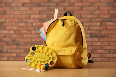 Photo of Yellow backpack with notebooks and art supplies on desk in classroom