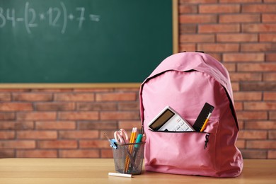 Photo of Pink backpack with different stationery on desk in classroom