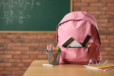 Photo of Pink backpack with different stationery on desk in classroom