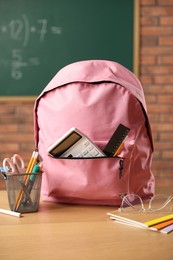Photo of Pink backpack with different stationery on desk in classroom