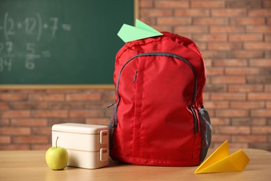 Photo of Backpack, lunchbox and apple on desk in classroom