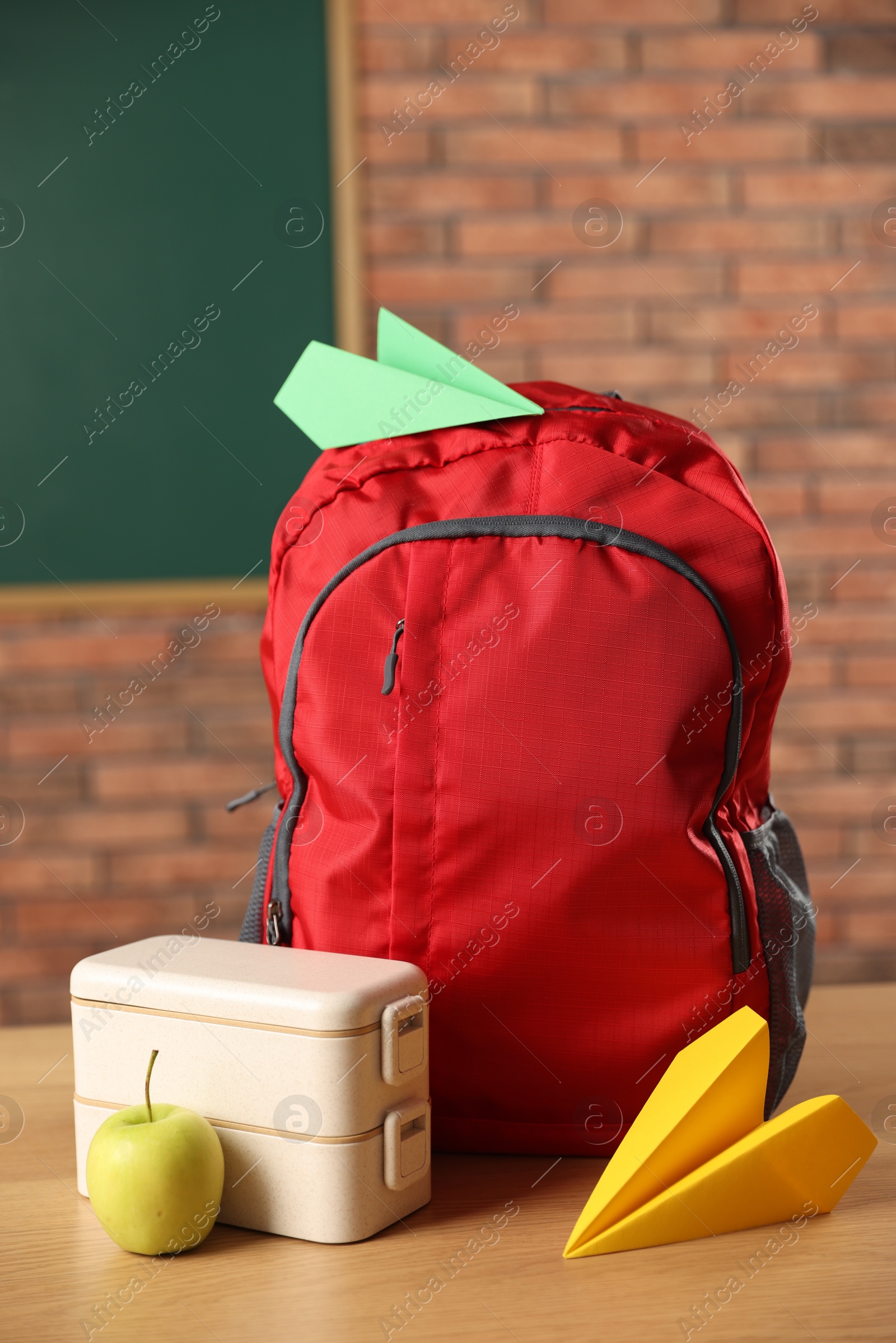 Photo of Backpack, lunchbox and apple on desk in classroom