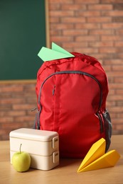 Photo of Backpack, lunchbox and apple on desk in classroom