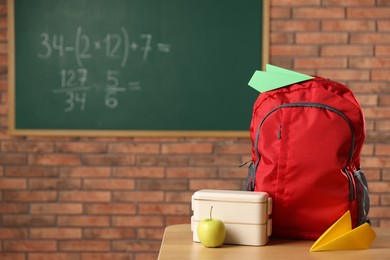 Photo of Backpack, lunchbox and apple on desk in classroom. Space for text