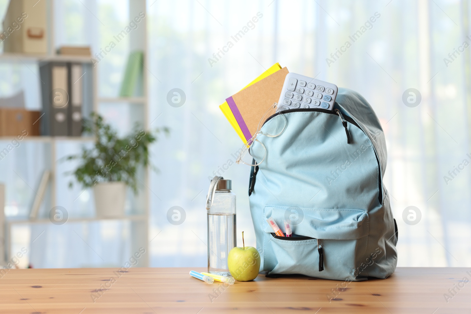 Photo of Backpack, different stationery, bottle of water and apple on desk in classroom. Space for text