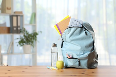 Photo of Backpack, different stationery, bottle of water and apple on desk in classroom. Space for text