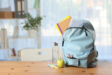 Photo of Backpack, different stationery, bottle of water and apple on desk in classroom. Space for text