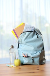 Photo of Backpack, different stationery, bottle of water and apple on desk in classroom