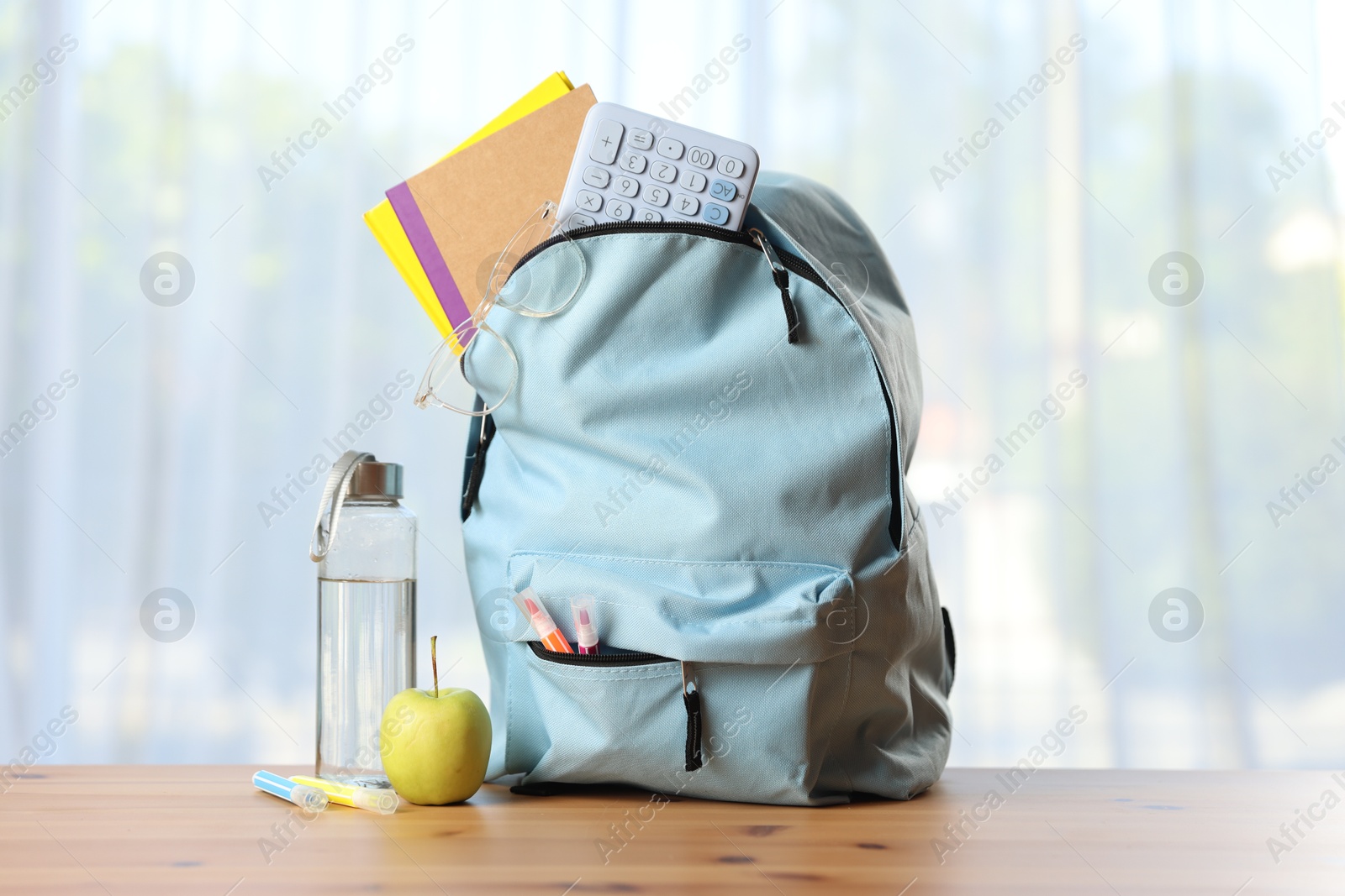 Photo of Backpack, different stationery, bottle of water and apple on desk in classroom