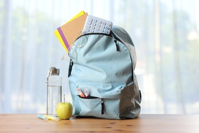 Photo of Backpack, different stationery, bottle of water and apple on desk in classroom