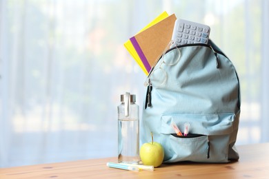 Photo of Backpack, different stationery, bottle of water and apple on desk in classroom. Space for text