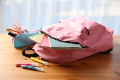 Photo of Backpack and different stationery on desk in classroom, closeup