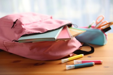 Photo of Backpack and different stationery on desk in classroom, closeup