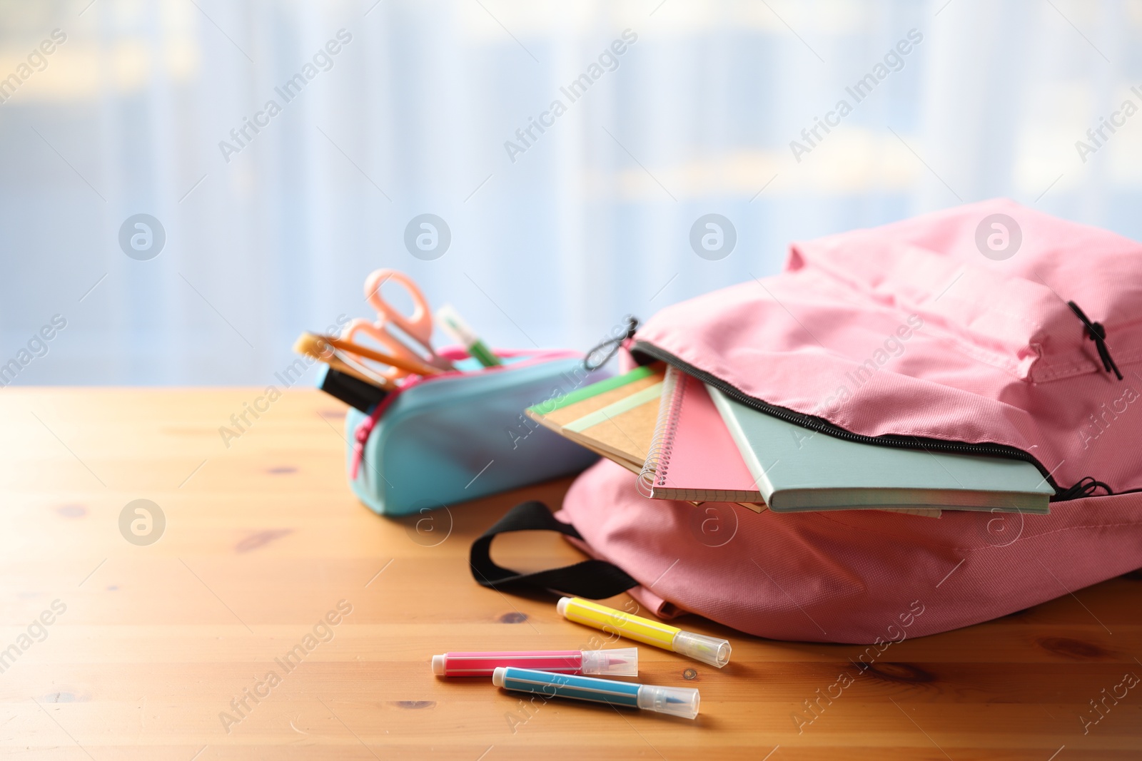 Photo of Backpack and different stationery on desk in classroom, closeup