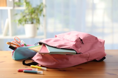 Photo of Backpack and different stationery on desk in classroom, closeup