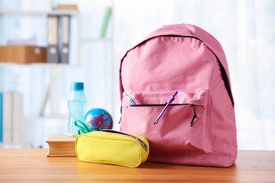 Photo of Backpack, different stationery, book and bottle of water on desk in classroom
