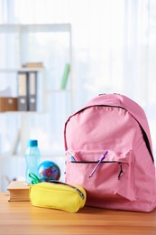 Photo of Backpack, different stationery, book and bottle of water on desk in classroom