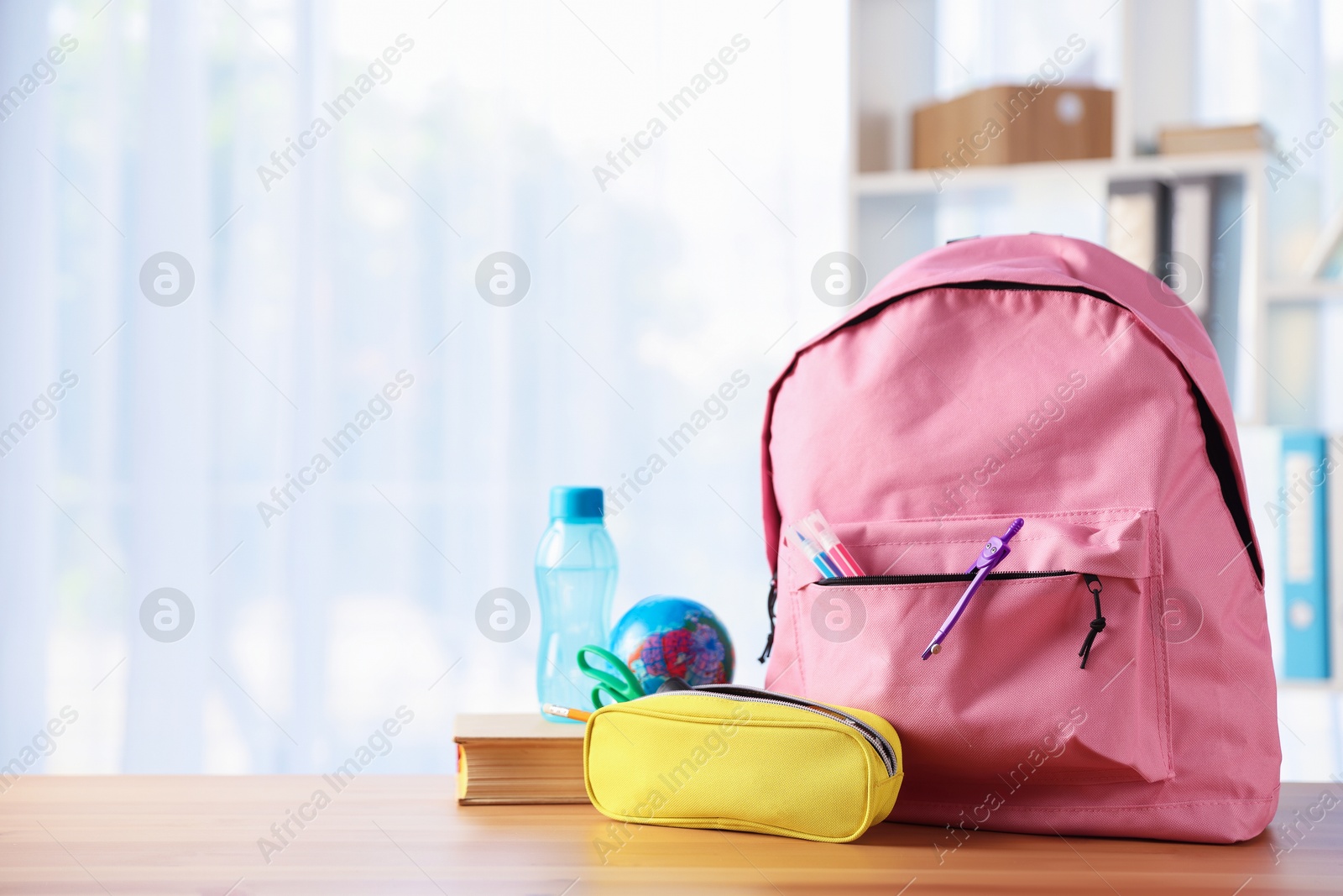 Photo of Backpack, different stationery, book and bottle of water on desk in classroom. Space for text