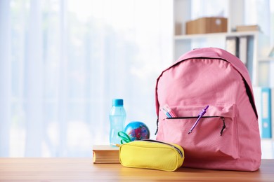 Photo of Backpack, different stationery, book and bottle of water on desk in classroom. Space for text