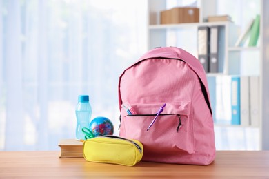 Photo of Backpack, different stationery, book and bottle of water on desk in classroom