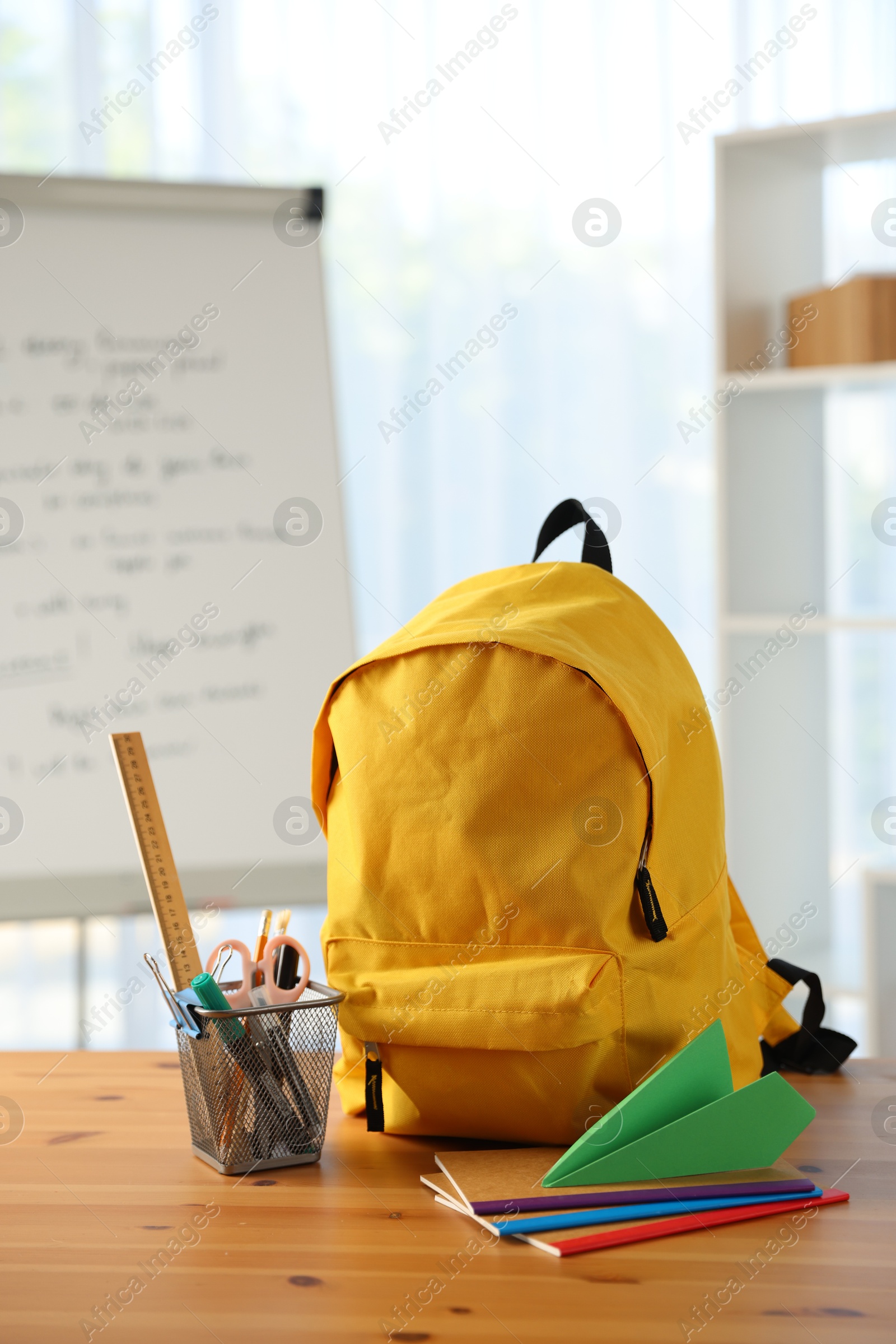 Photo of Backpack, different stationery and paper plane on desk in classroom