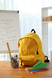 Photo of Backpack, different stationery and paper plane on desk in classroom