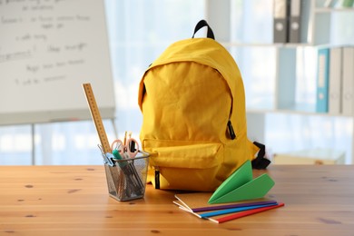 Photo of Backpack, different stationery and paper plane on desk in classroom