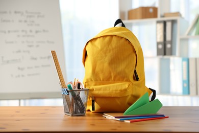 Photo of Backpack, different stationery and paper plane on desk in classroom