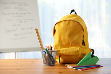 Photo of Backpack, different stationery and paper plane on desk in classroom