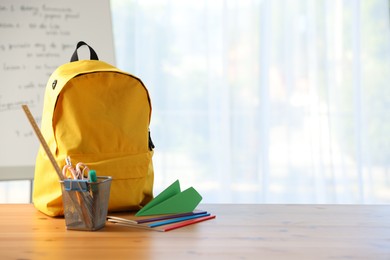 Photo of Backpack, different stationery and paper plane on desk in classroom. Space for text
