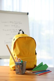 Photo of Backpack, different stationery and paper plane on desk in classroom
