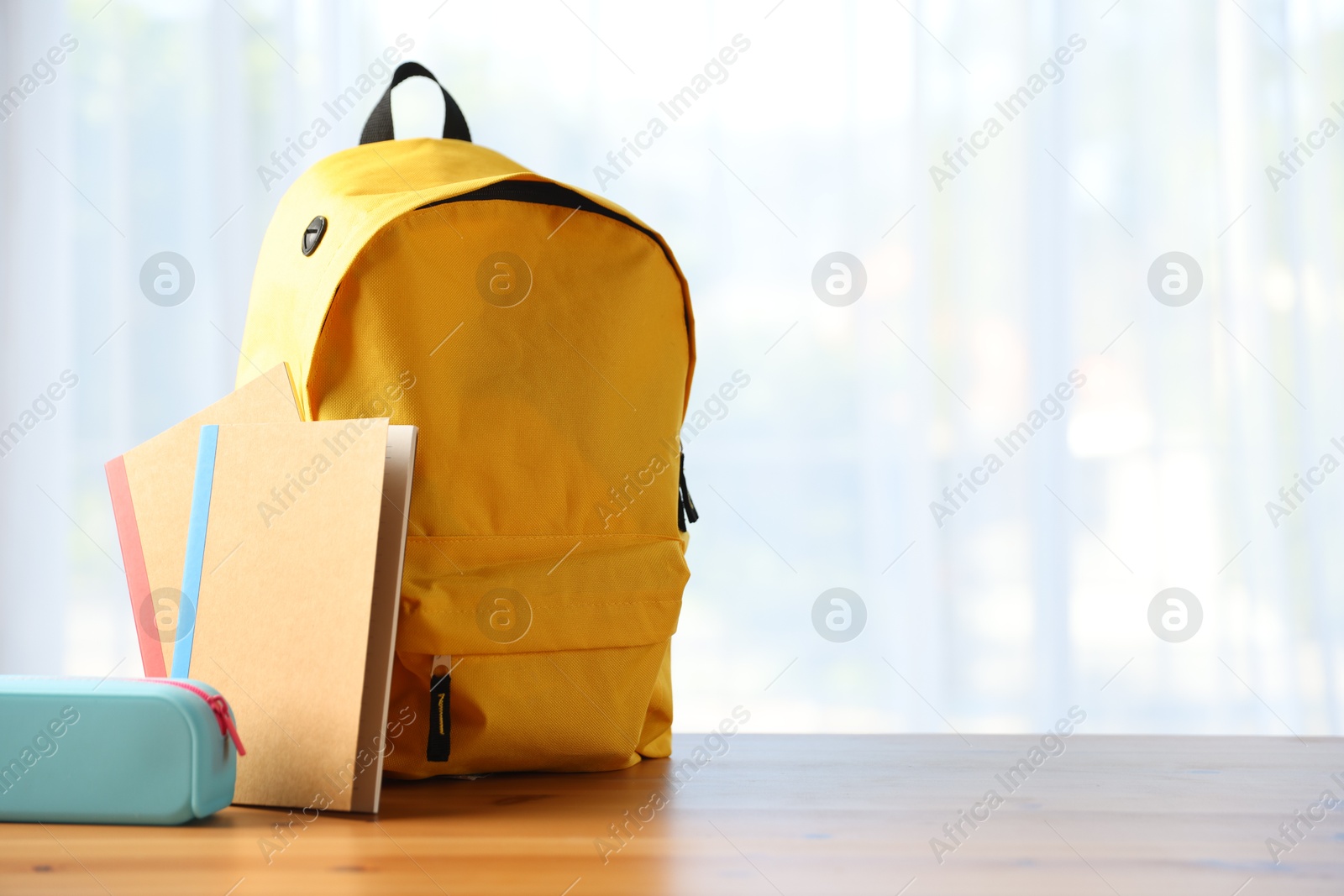 Photo of Backpack, notebooks and pencil case on desk in classroom. Space for text