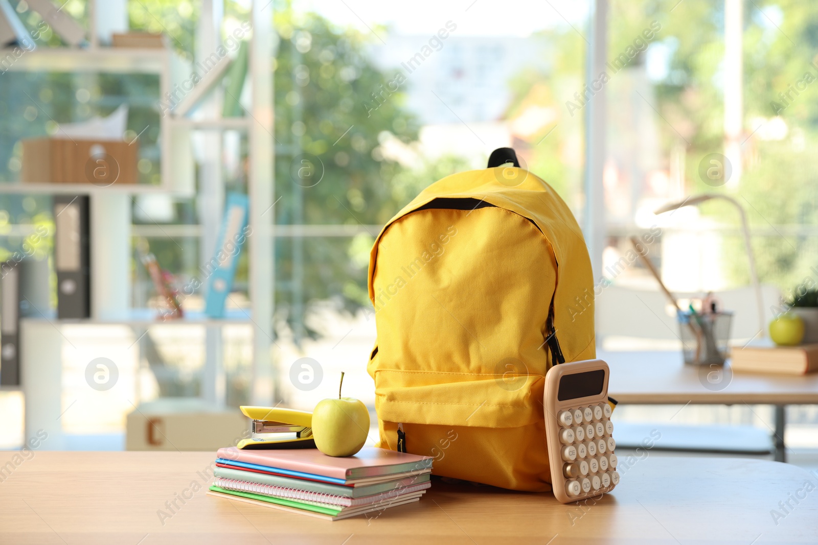Photo of Backpack, different stationery and apple on desk in classroom