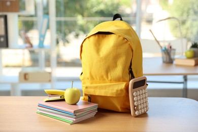 Photo of Backpack, different stationery and apple on desk in classroom