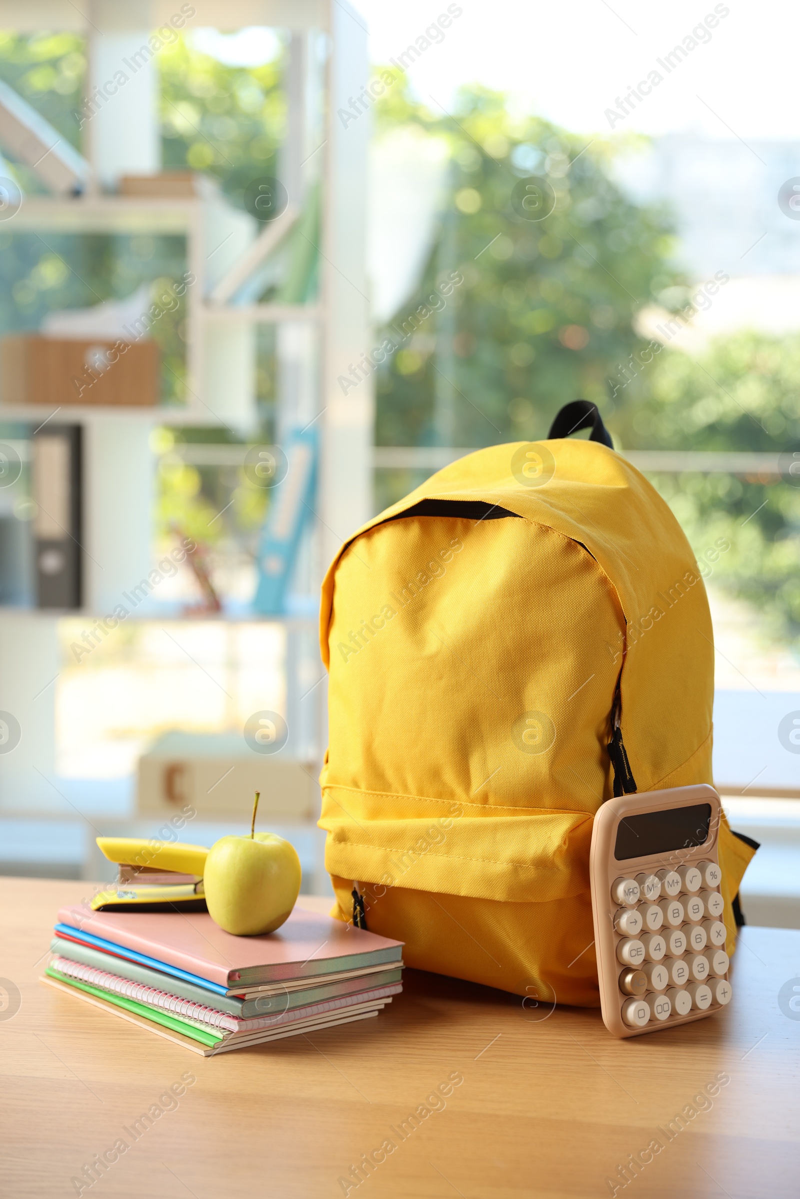 Photo of Backpack, different stationery and apple on desk in classroom