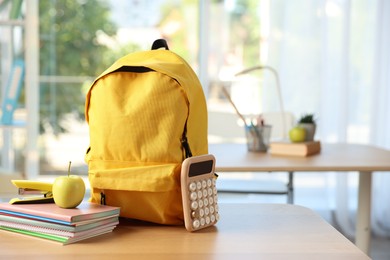 Photo of Backpack, different stationery and apple on desk in classroom. Space for text