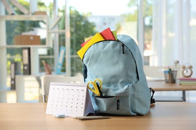 Photo of Backpack with different stationery and calendar on desk in classroom