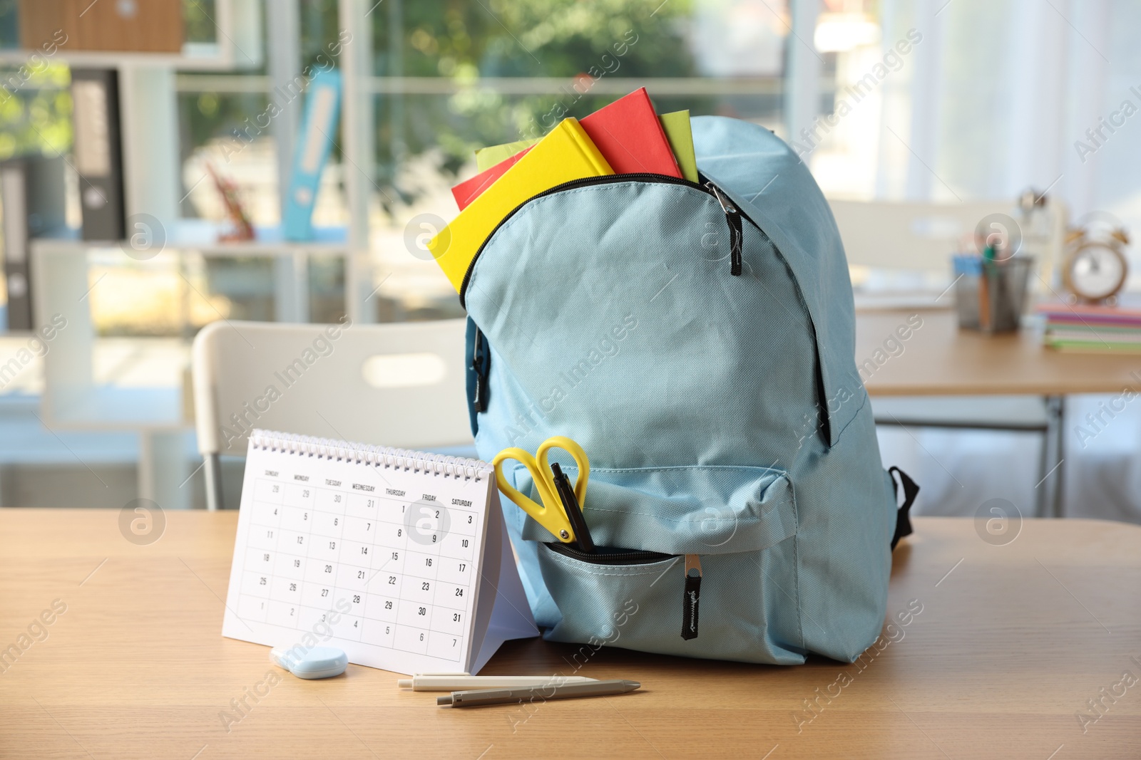 Photo of Backpack with different stationery and calendar on desk in classroom
